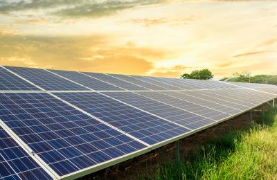 Solar panels installed on a grassy field under a vibrant sunset sky, symbolizing renewable energy.